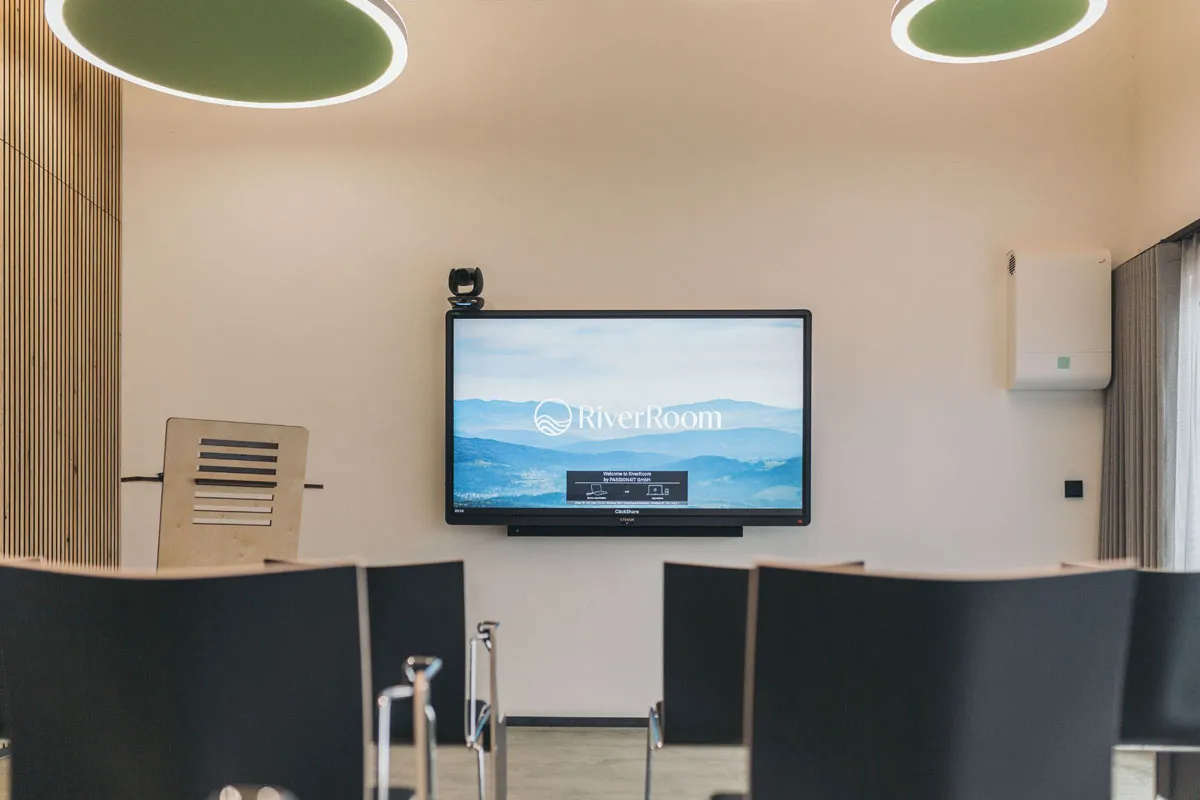 75-inch OLED TV showing the RiverRoom logo, with the lectern next to it